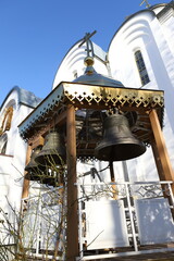 Small snow-covered bell tower with silver bells on the background of the Orthodox Church. Winter, Christmas. The concept of Orthodoxy.