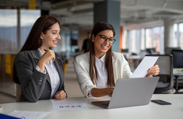 Two successful women are working on a laptop in the office.