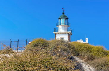 Fototapeta na wymiar The lighthouse at Akortiri peeps up above a dune in Santorini in summertime
