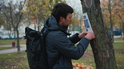 The man has lost his best friend a husky puppy. The owner posts an ad banner about the missing dog on the trees in the park. Missing pet banner. Dog search reward. Stole a pet. Lost Siberian Husky