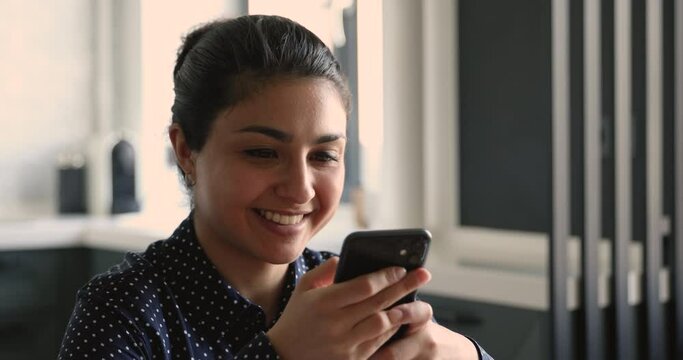 Close up head shot smiling young beautiful indian mixed race woman holding cellphone, using mobile applications, chatting with friends in social networks, playing online game, web surfing or shopping.