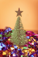 Small green toy fir tree with star against defocused christmas decoration