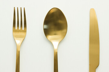 Golden cutlery on white background; symmetrical; spoon, knife and fork