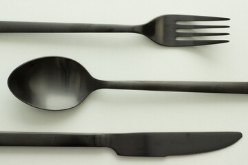 Close up of black cutlery on white background; spoon, knife and fork; dishware; abstract