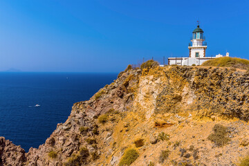 Fototapeta na wymiar A view of the lighthouse at Akortiri at the end of the caldera rim in Santorini in summertime