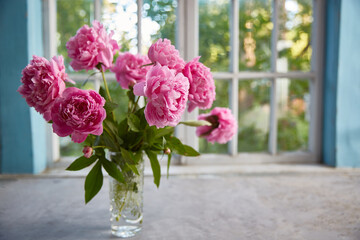 Peonies in a vase on the table against the background of the window.