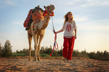 Eine blonde Frau geht mit einem Kamel an der Leine durch die Wüste von Ägypten