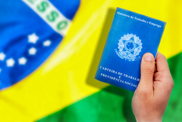 Jovem segurando carteira de trabalho brasileira com a bandeira do Brasil no fundo (CTPS). Pessoa em...