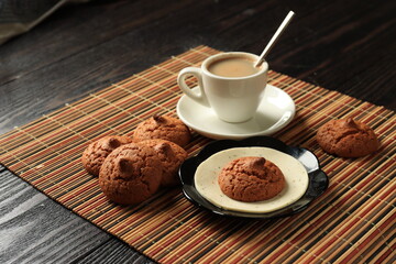 Oatmeal cookies and white cup with coffee on bamboo napkin