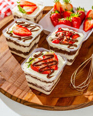 Bolos de pote caseiros sobre mesa de madeira com cobertura de chocolate e morangos.