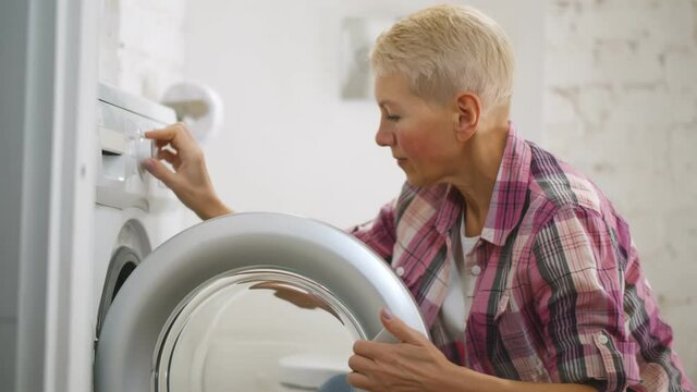 Attractive senior woman doing laundry in bathroom at home