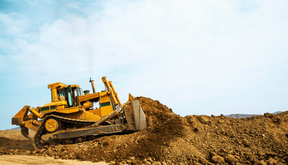 Bulldozer at a construction site shovels mountain soil into a heap.