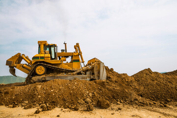 Fototapeta na wymiar Bulldozer at a construction site shovels mountain soil into a heap.