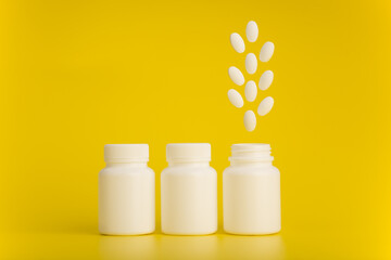 Three medicine bottles in a row with pills floating above the last one. Creative concept of vitamins, supplement, healthcare and wellbeing