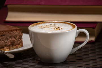 Cup of cappuccino with a slice of cake on the background of the book
