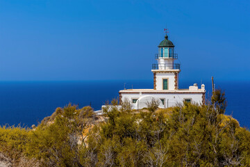 Fototapeta na wymiar A view past trees towards the lighthouse at Akortiri in Santorini in summertime