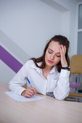 A beautiful young woman sits at a table and signs important documents.