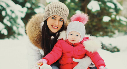 Portrait of happy smiling mother and little child in winter day together over snowy background