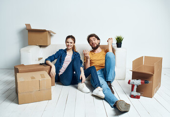 Fototapeta na wymiar moving renovation happy man and woman on the floor in a new apartment with boxes