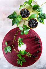 Pastila of black currant berries on a light background. Nearby is a branch with green leaves. Black currants in ceramic dishes.