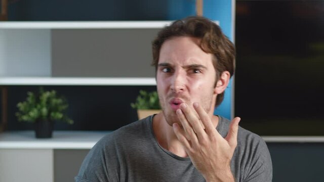 Shocked young man shows disgust at what he sees. The unpleasantly surprised male covers his mouth with his hand. Home or office apartment on background