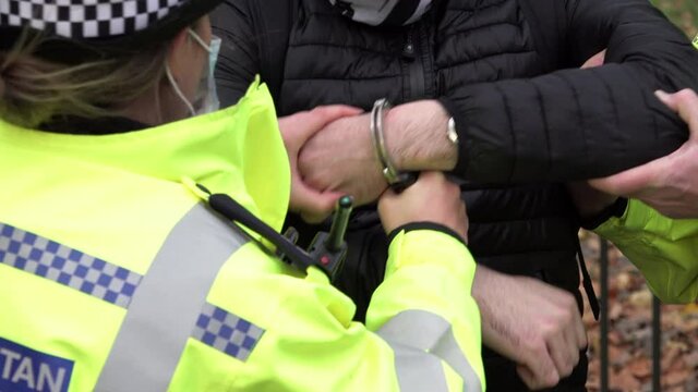 A police officer holds on to the handcuffs being used to restrain an arrestee.
