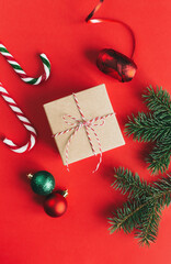 Gift box with spruce branches, balls and candy canes on a red background.