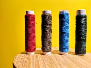 four bobbins of colored threads on a yellow background