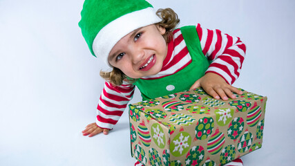 Little elf with a cute smile is sitting on the white background and playing or packing Christmas presents. Christmas holiday background photo.