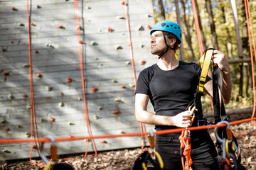 Handsome man wearing safety equipment for climbing at amusement park, preparing for climbing on the wall