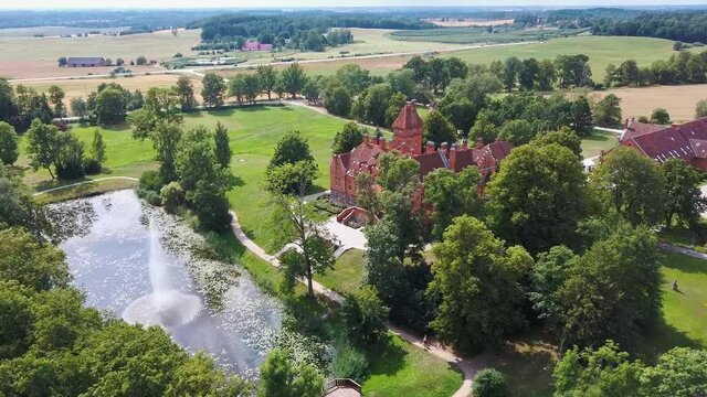 Jaunmoku Brick Medieval Castle Near Tukums, Latvia  at Pond in Clear Sunny Summer Day From Above Top View. The Jaunmokas Manor Park. Aerial Dron 4k Shot