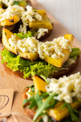 Toasted sandwiches with brie cheese, baked pumpkin and salad, arugula and mozzarella, delicious vegetable snacks on a wooden board