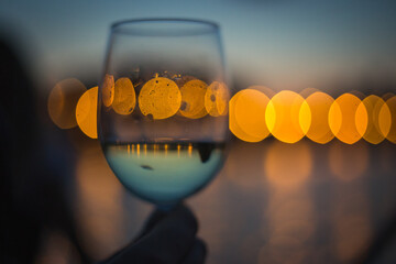 bokeh lights in a glass of white wine, reflection of city lights and sky in the glass upside down - 395830224