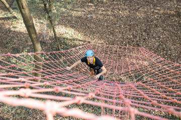 Well-equipped man climbing on a net outdoors, having active recreation in amusement park