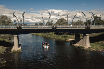 bridge over the river Gauja during the day blue sky white clouds and the boat with a red roof 