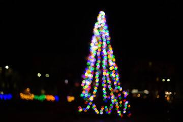 silhouette of colorful wreaths in the shape of a Christmas tree with space for text. Blurred abstract bright spot lights isolated on dark background. new year and christmas bright background 