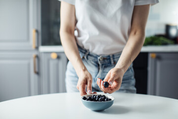 Woman's hands take blueberries from the plate. On the background of a beautiful kitchen.