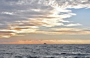 Seascape with gray sea, cloudy sky and ship on the horizon during sunset