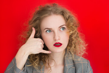 Young surprise woman with curly hair over red wall making phone gesture. Call me back sign. Communication symbols.