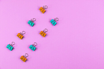 Stationery set, multi-colored paper clips lined up, flat lay, copy space, pink background