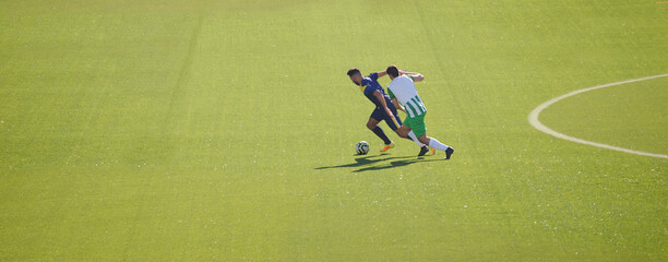 Dois jogadores de equipas diferentes a disputar a bola em jogo - equipamentos verde e branco e azul - meio campo - futebol © ajcsm