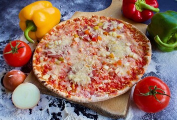 Homemade Pepperoni Pizza with Cheese, fresh tomatoes, red yellow green peppers and onion. Served on a wooden peel on a black background with flour on the surface
