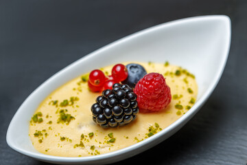 Dessert of whipped cream, raspberries, blueberries, blackberries and red currants in a porcelain tray close-up.