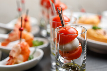 Cherry tomatoes and mozzarella canapes on skewers in a glass glass with a background of king prawns in close-up