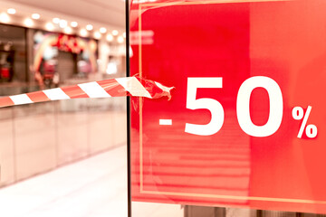 Sale - 50%. Shop window in mall with red signboard and signal tape. Closed shopping center. Quarantine measures