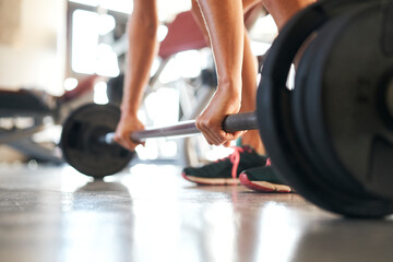 Close up of fit young woman lifting barbells looking focused, working out in a gym alone.