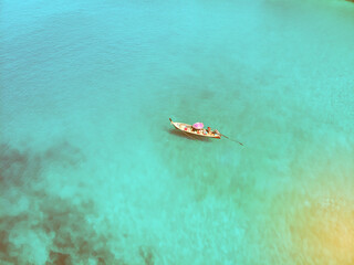 Aerial view of the wooden Thai boat with a pink parasol sailing the immensely clear sea, tourism; paradise concept.