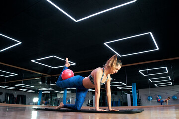 A Caucasian woman exercising pilates fitness ball exercises in a modern gym.
