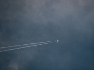 jet plane with white fuselage, flying at high altitude under a cloudy sky, leaving a white trail of steam.