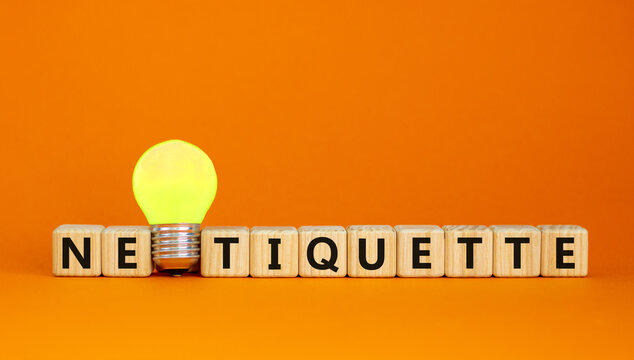 Symbol for netoquette time. Wooden cubes with word 'netiquette'. Yellow light bulb. Beautiful orange background. Copy space. Business and netiquette concept.
